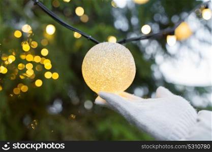 holidays and decoration concept - close up of hand with christmas tree garland bulb outdoors. close up of hand with christmas tree garland bulb