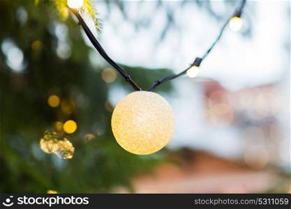 holidays and decoration concept - close up of natural fir with christmas tree garland bulb outdoors. close up of fir with christmas tree toys outdoors