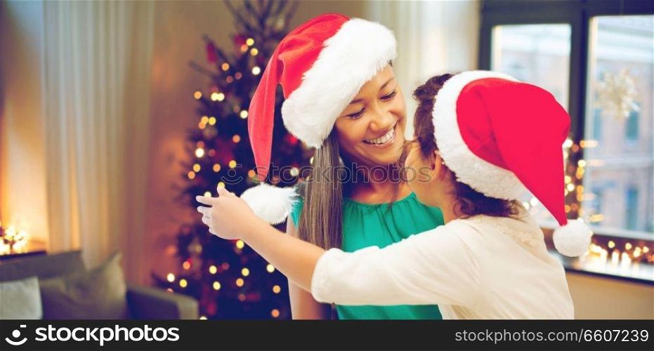 holidays and family concept - happy mother and daughter in santa hats over room with christmas tree background. happy mother and daughter on christmas