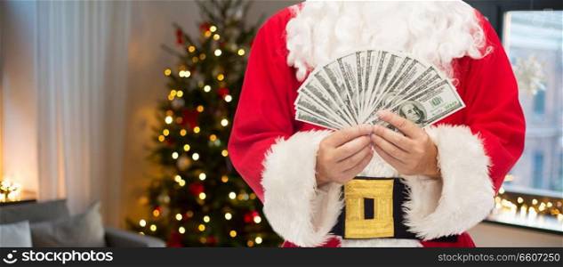 holidays and finance concept - close up of santa claus with dollar money over room with christmas tree background. close up of santa claus with dollar money