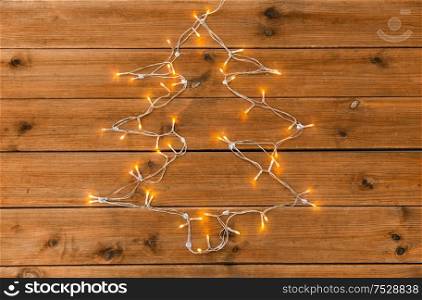 holidays and illumination concept - electric garland lights string in shape of christmas tree on wooden background. garland lights string in shape of christmas tree