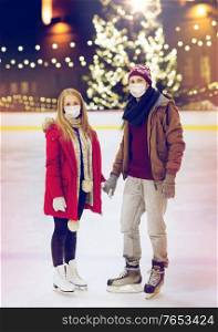 holidays and leisure concept - couple wearing face protective medical masks for protection from virus disease holding hands at outdoor skating rink over christmas tree background. couple in masks holding hands on skating rink