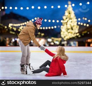 holidays and leisure concept - smiling man helping woman to rise up on outdoo skating rink over christmas tree background. man helping woman on christmas skating rink