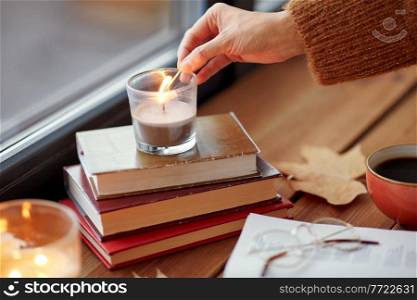 holidays and leisure concept - woman&rsquo;s hand with match lighting candle at home on halloween. hand with match lighting candle on window sill