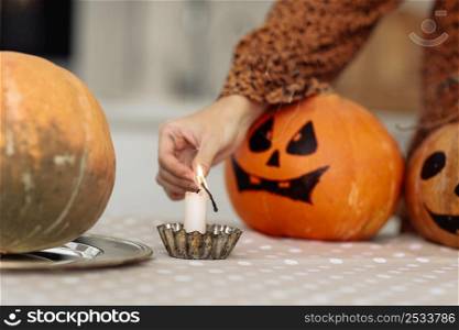 holidays and leisure concept - woman&rsquo;s hand with matches lighting candles at home on halloween. painted pumpkins on a background. horror theme and Hallowe&rsquo;en. selective focus. holidays and leisure concept - woman&rsquo;s hand with matches lighting candles at home on halloween. painted pumpkins on a background. horror theme and Hallowe&rsquo;en. selective focus.