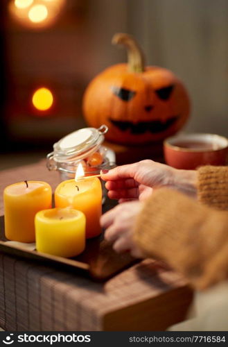 holidays and leisure concept - woman’s hand with match lighting candle at home on halloween. hand with match lighting candle on halloween
