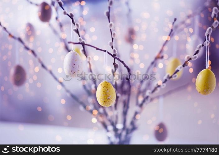 holidays and object concept - close up of pussy willow branches decorated by easter eggs in violet shades over festive lights. close up of pussy willow decorated by easter eggs