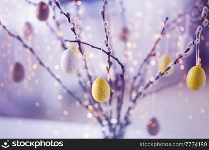 holidays and object concept - close up of pussy willow branches decorated by easter eggs in violet shades over festive lights. close up of pussy willow decorated by easter eggs