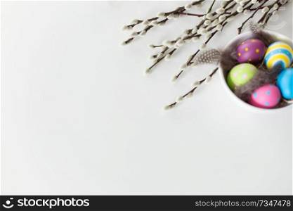 holidays and object concept - colored easter eggs with quail feathers in bowl and pussy willow branches on white background. colored easter eggs and pussy willow branches