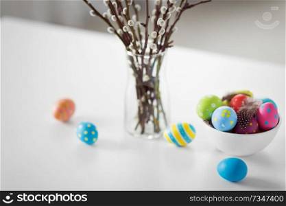 holidays and object concept - pussy willow branches and colored easter eggs in vase on table. pussy willow branches and colored easter eggs
