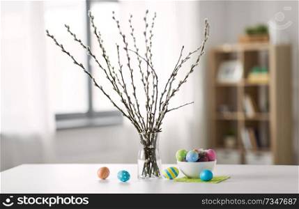 holidays and object concept - pussy willow branches and colored easter eggs in vase on table. pussy willow branches and colored easter eggs