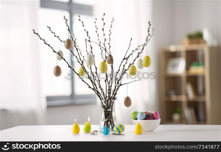 holidays and object concept - pussy willow branches decorated by easter eggs in vase and candles on table. pussy willow branches decorated by easter eggs