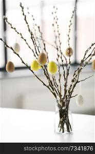 holidays and object concept - pussy willow branches decorated by easter eggs in vase on table. pussy willow branches decorated by easter eggs