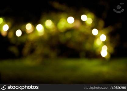 holidays and party concept - blurred garland lights at night summer garden background. garland lights at night summer garden background