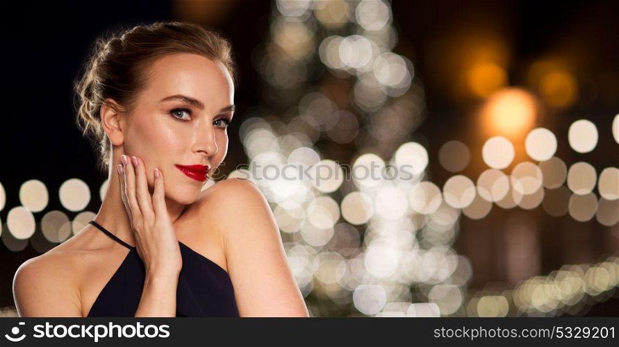 holidays and people concept - beautiful woman in black with red lips over christmas tree lights background. beautiful woman over christmas tree lights