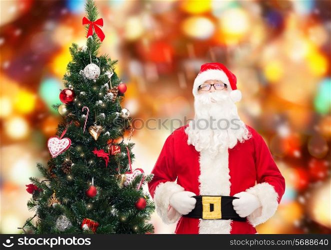 holidays and people concept concept - man in costume of santa claus with christmas tree over red lights background