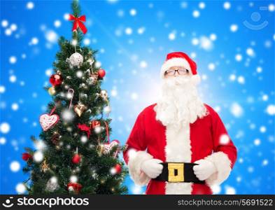 holidays and people concept concept - man in costume of santa claus with christmas tree over blue snowy background