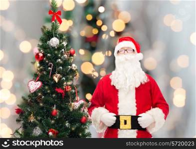 holidays and people concept concept - man in costume of santa claus with christmas tree over lights background