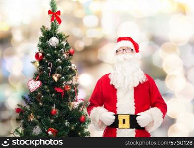 holidays and people concept concept - man in costume of santa claus with christmas tree over lights background
