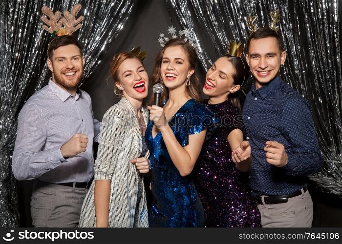 holidays and people concept - happy friends with microphone singing karaoke at christmas party. friends with microphone singing at christmas party