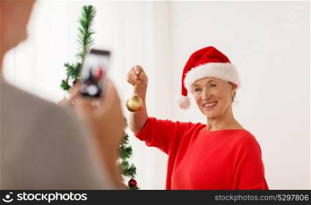 holidays and people concept - happy senior woman decorating christmas tree and posing for photo. happy senior woman decorating christmas tree