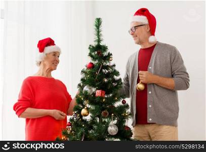 holidays and people concept - happy smiling senior couple in santa hats decorating christmas tree at home. happy senior couple decorating christmas tree
