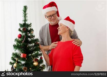 holidays and people concept - happy smiling senior couple in santa hats at christmas tree. happy senior couple at christmas tree