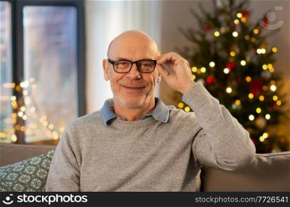 holidays and people concept - happy smiling senior man in glasses at home in evening over christmas tree lights on background. happy smiling senior man in glasses on christmas