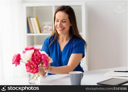 holidays and people concept - happy smiling woman setting flowers in vase on office table. woman setting flowers in vase on office table