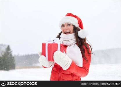 holidays and people concept - happy woman in santa hat with chrismas gift outdoors in winter. happy woman in santa hat with chrismas gift