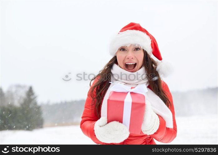holidays and people concept - happy woman in santa hat with chrismas gift outdoors in winter. happy woman in santa hat with chrismas gift