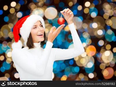 holidays and people concept - happy woman in santa hat with christmas ball over lights background. happy woman in santa hat with christmas ball