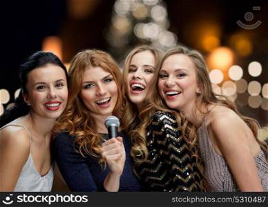 holidays and people concept - happy women with microphone singing karaoke at new year party over christmas tree lights background. women with microphone singing karaoke at christmas