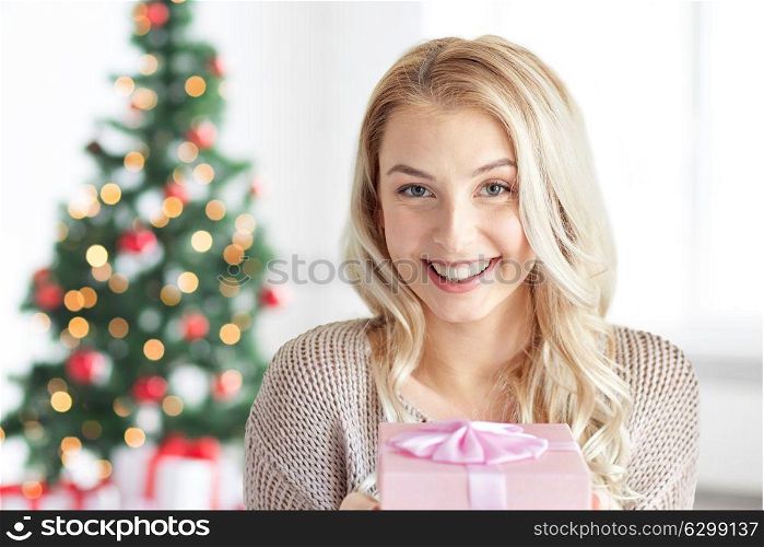 holidays and people concept - happy young woman gift box or present at home over christmas tree background. happy young woman with gift box at christmas