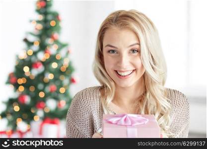 holidays and people concept - happy young woman gift box or present at home over christmas tree background. happy young woman with gift box at christmas