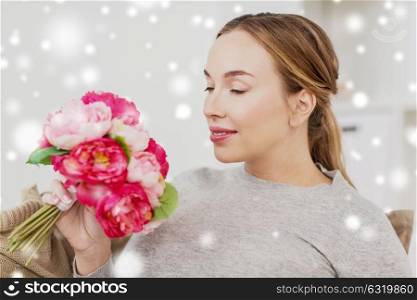 holidays and people concept - happy young woman smelling flowers at home over snow. happy woman smelling flowers at home