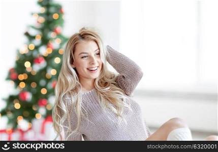 holidays and people concept - happy young woman stretching in bed at home bedroom over christmas tree background. happy young woman stretching in bed at christmas