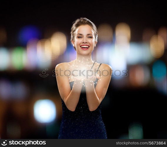 holidays and people concept - laughing woman in evening dress holding something over night lights background