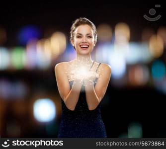 holidays and people concept - laughing woman in evening dress holding something over night lights background