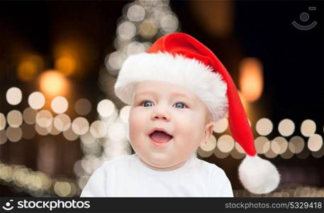 holidays and people concept - little baby boy in santa hat over christmas tree background. little baby boy in santa hat at christmas