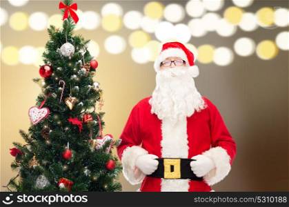 holidays and people concept - man in costume of santa claus at christmas tree over lights background. santa claus at christmas tree