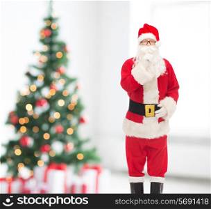holidays and people concept - man in costume of santa claus making hush gesture over snowy city background over living room and christmas tree background