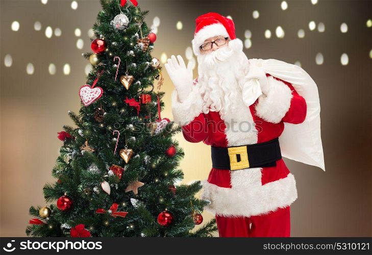 holidays and people concept - man in costume of santa claus with bag and christmas tree waving hand. santa claus with bag and christmas tree
