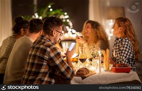 holidays and people concept - man with smartphone at dinner party with friends at home. man with smartphone at dinner party with friends