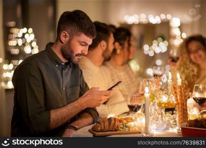 holidays and people concept - man with smartphone at dinner party with friends at home. man with smartphone at dinner party with friends
