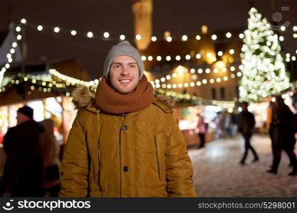 holidays and people concept - portrait of beautiful happy young man at christmas market in winter evening. happy young man at christmas market in winter