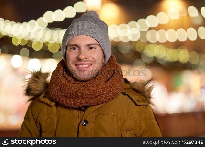 holidays and people concept - portrait of beautiful happy young man over christmas lights in winter evening. happy young man over christmas lights in winter