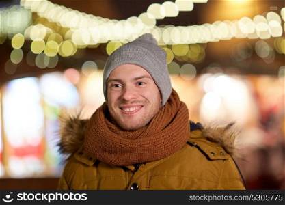 holidays and people concept - portrait of beautiful happy young man over christmas lights in winter evening. happy young man over christmas lights in winter
