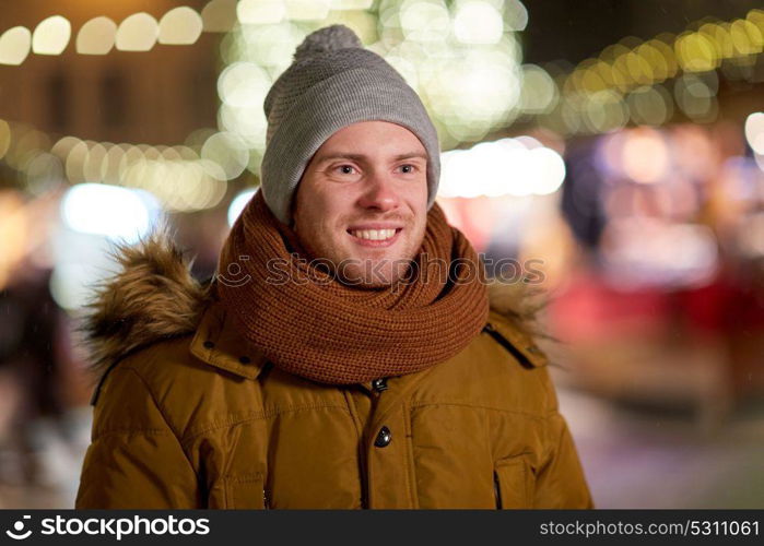 holidays and people concept - portrait of beautiful happy young man over christmas lights in winter evening. happy young man over christmas lights in winter