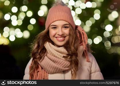 holidays and people concept - portrait of beautiful happy young woman over christmas tree lights in winter evening. happy young woman over christmas tree lights